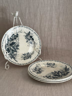 Four French green transferware luncheon plates in a blackberry pattern, one upright on a white iron plate stand and three stacked on a linen cloth