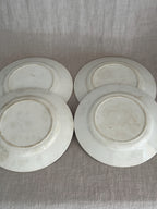 Undersides of four unmarked French luncheon plates laid out on linen, cream glaze with light age staining and impressed mould numbers