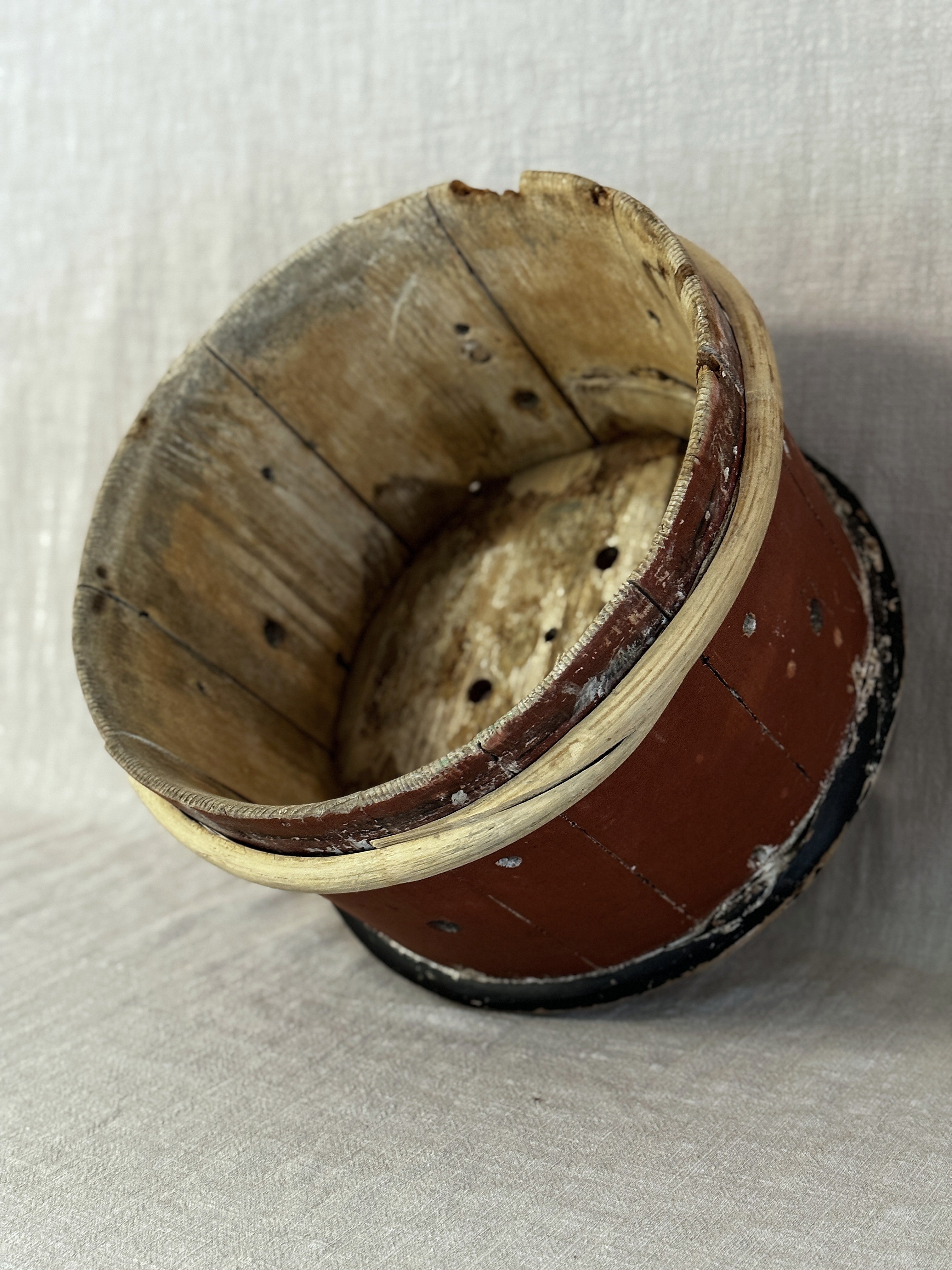 Side view of the Swedish cheese mould showing the painted staves, drainage holes and worn falu-red surface